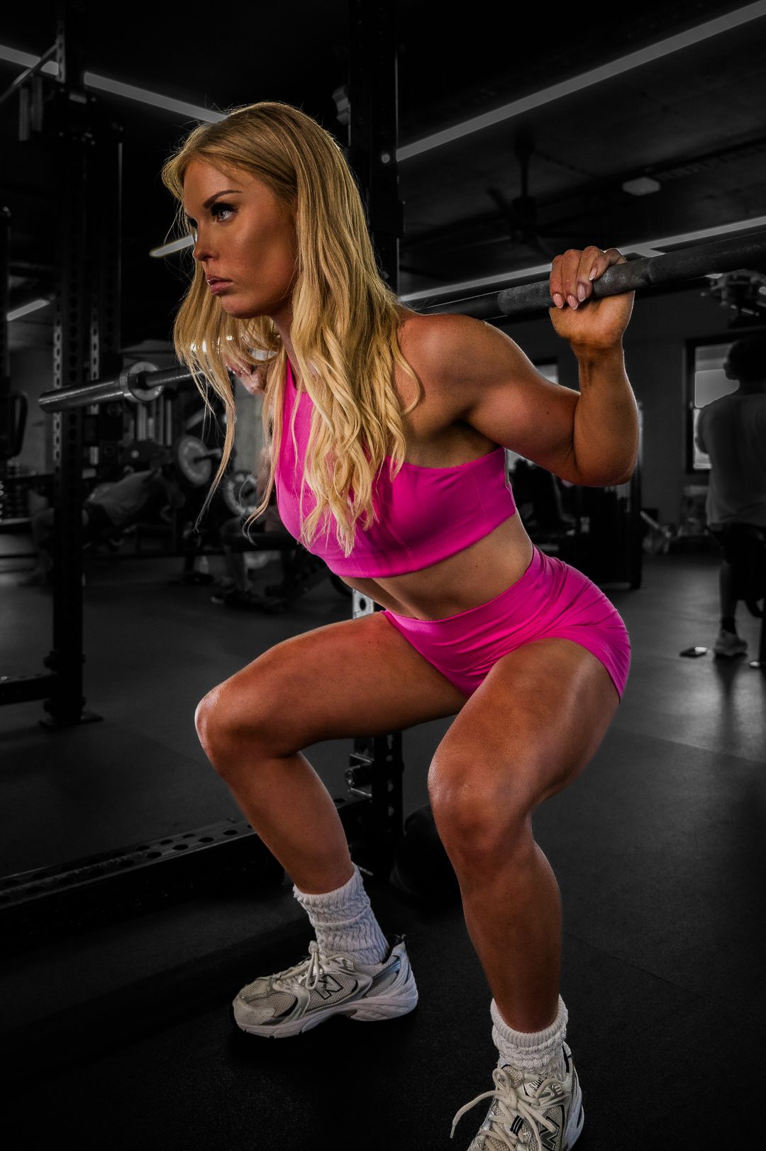 Strong athlete in pink workout gear performing weighted squats at the gym.