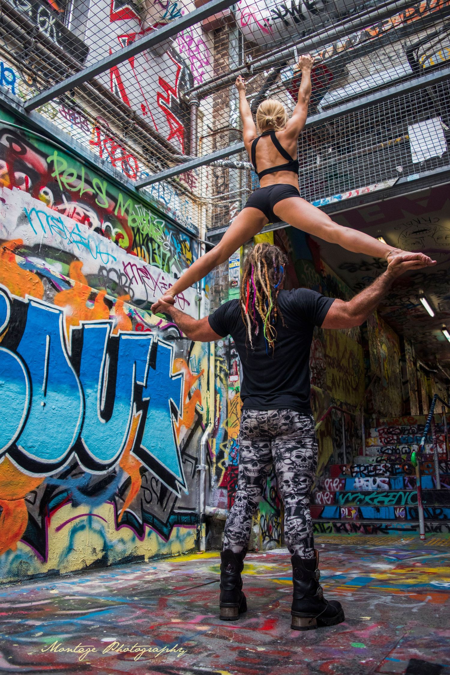 Acrobatic dance performance in vibrant graffiti-filled urban space shows impressive lift.