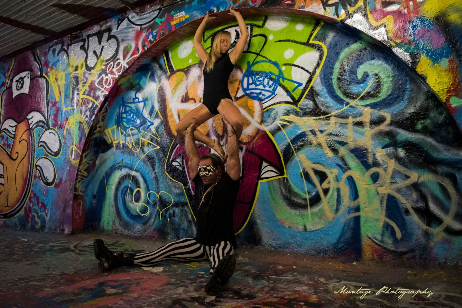 Dynamic partner dance lift photographed against colorful graffiti mural background.