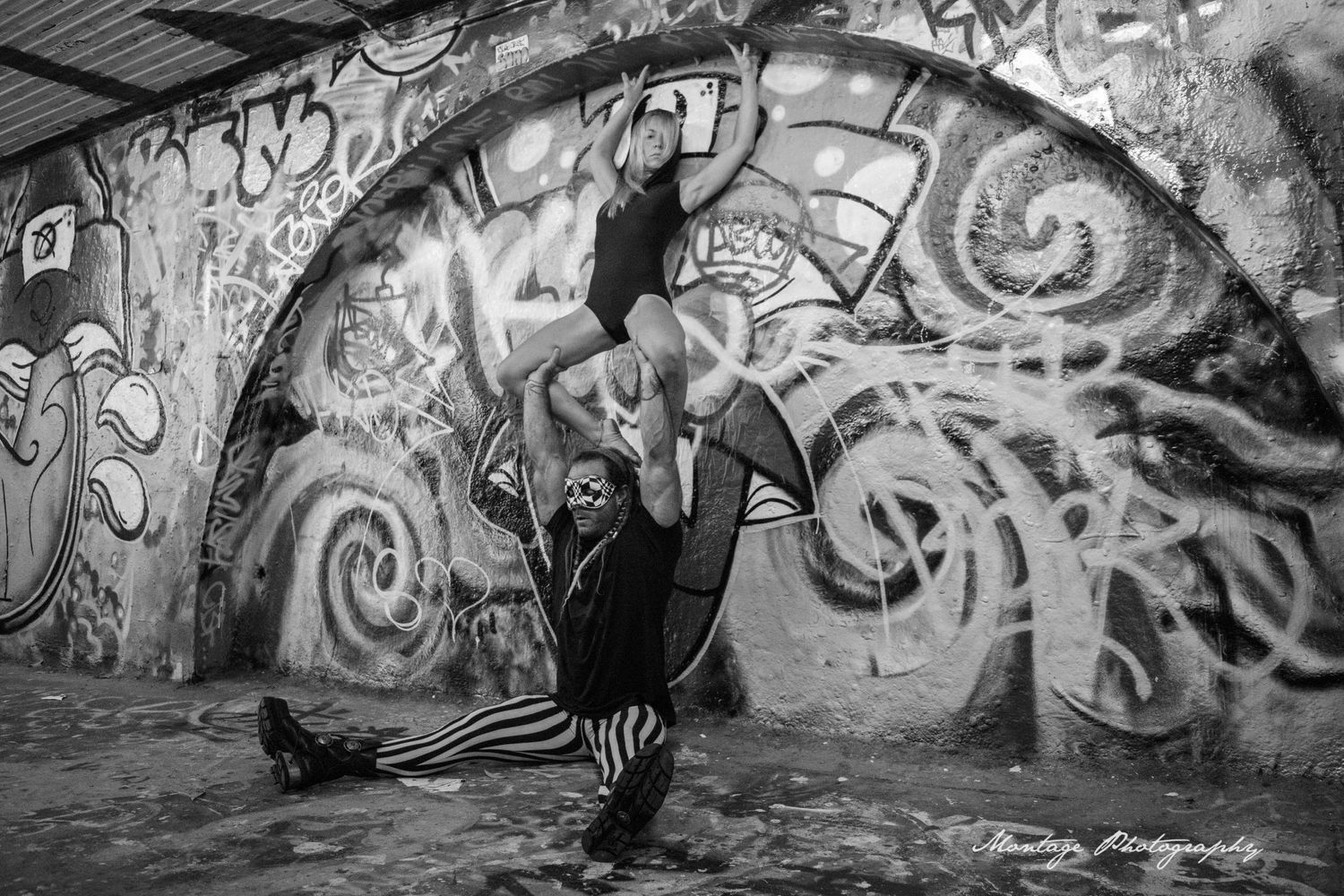 Black and white capture of artistic dance lift in graffiti-decorated urban setting.
