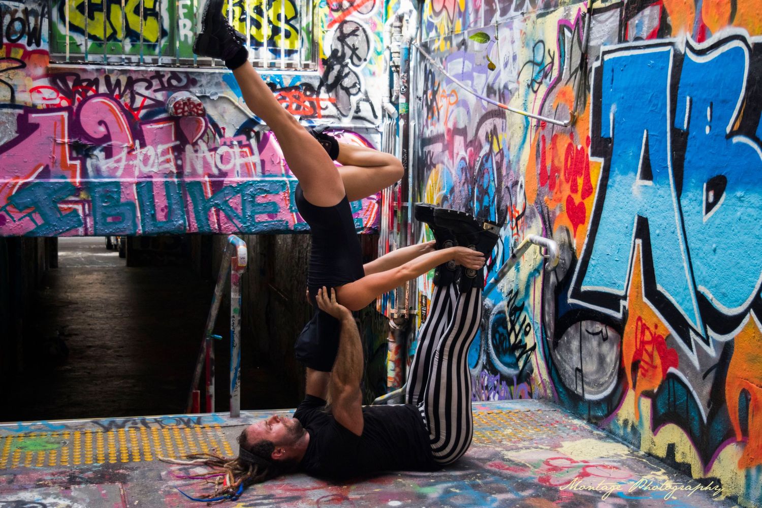 Athletic duo performs acrobatic dance move in front of colorful urban graffiti wall.