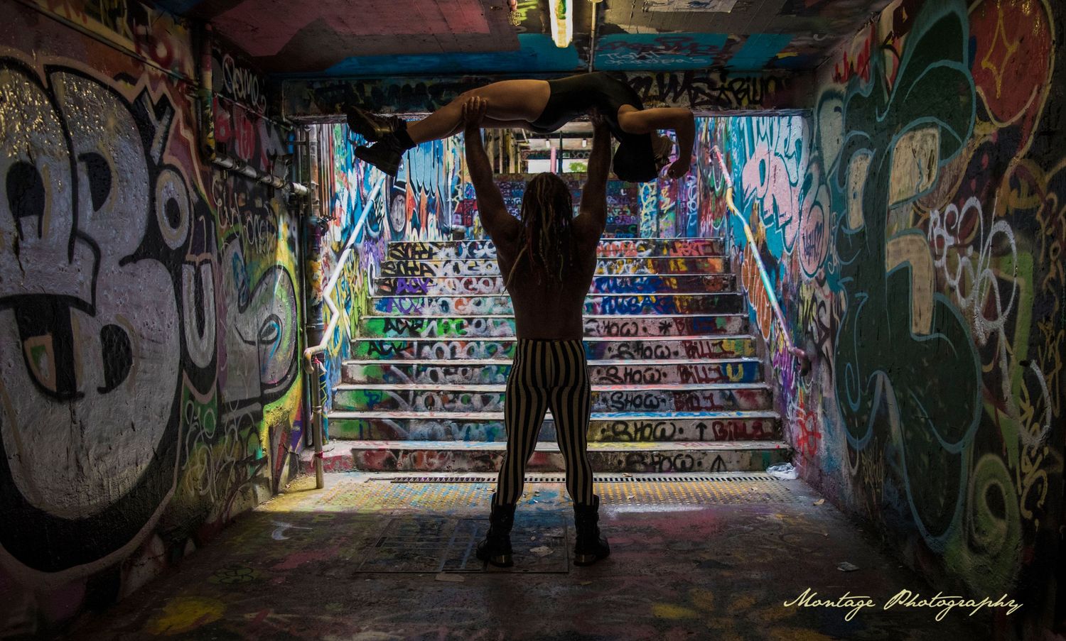 Silhouetted figures perform in graffiti tunnel with dramatic stair perspective.