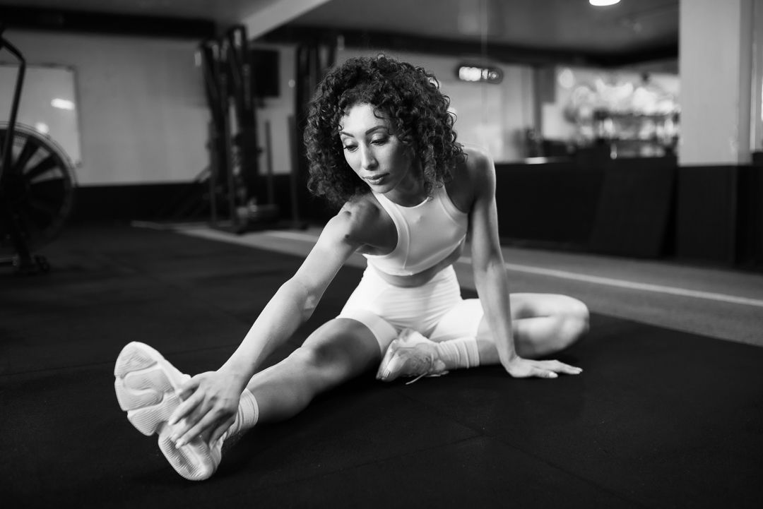 Athletic woman in white workout attire stretching on dark gym floor during fitness session.