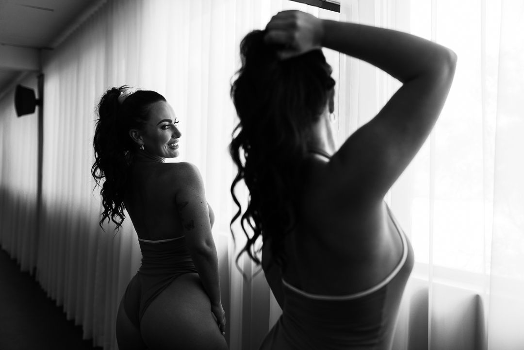Black and white artistic silhouette of figure posing beside mirror in studio setting.