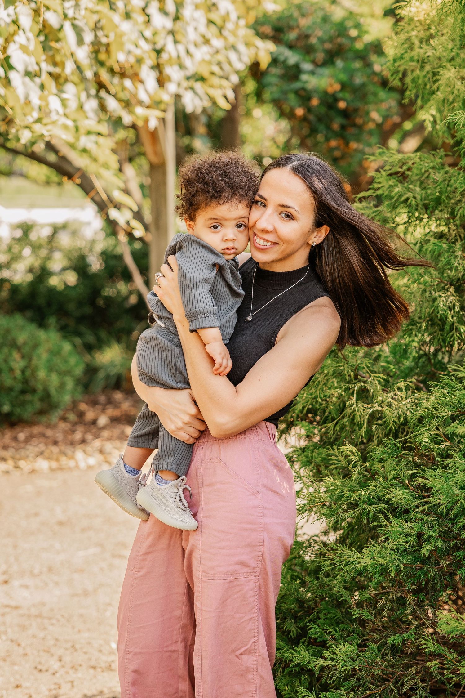 Parent holding small child against garden backdrop in casual summer outfits.