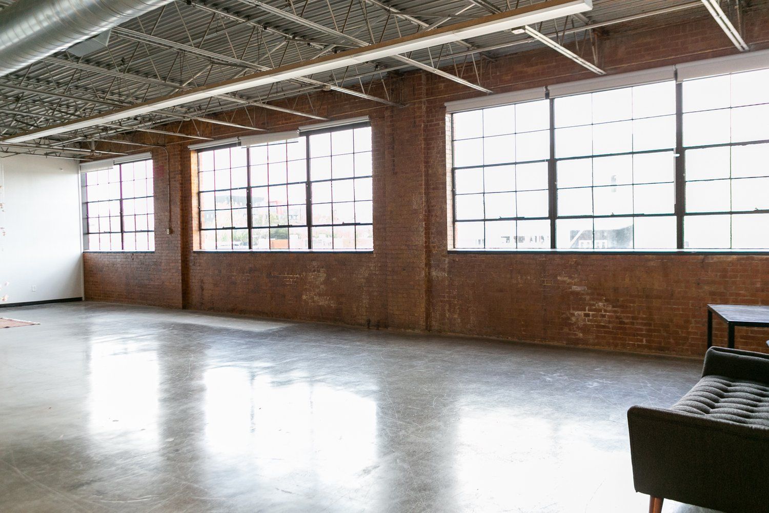 The inside of the modern boudoir photography studio has a brick wall, 3 west facing windows, & finished concrete floors