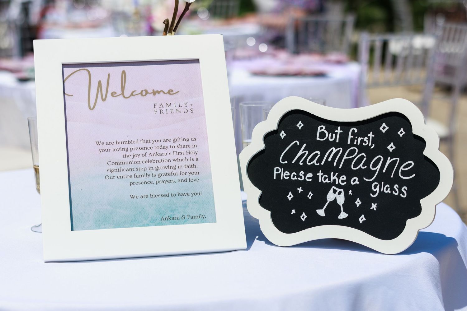 A welcome sign and chalkboard with champagne message displayed on a white table.
