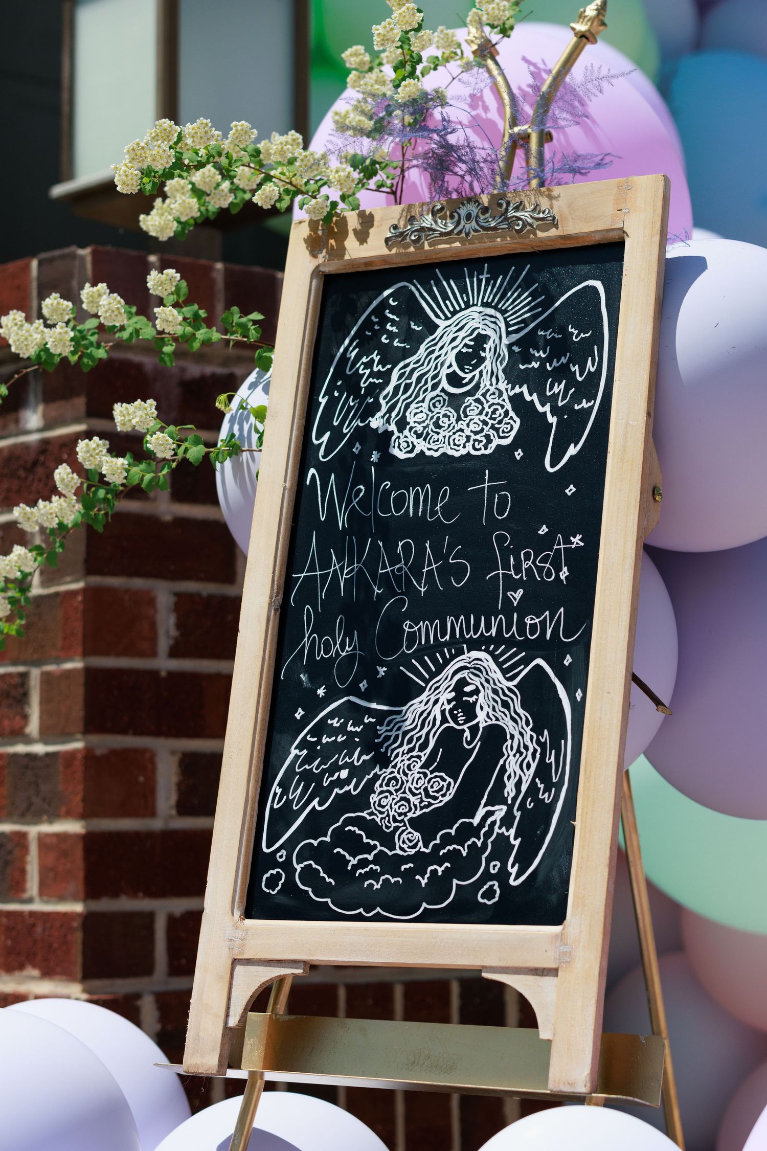 Decorative chalkboard welcome sign with angel drawings and purple balloons.