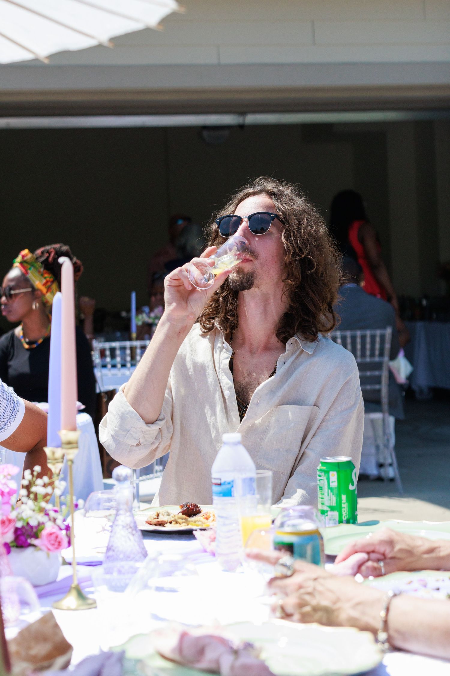 A person enjoying food at an outdoor party table with drinks and place settings.