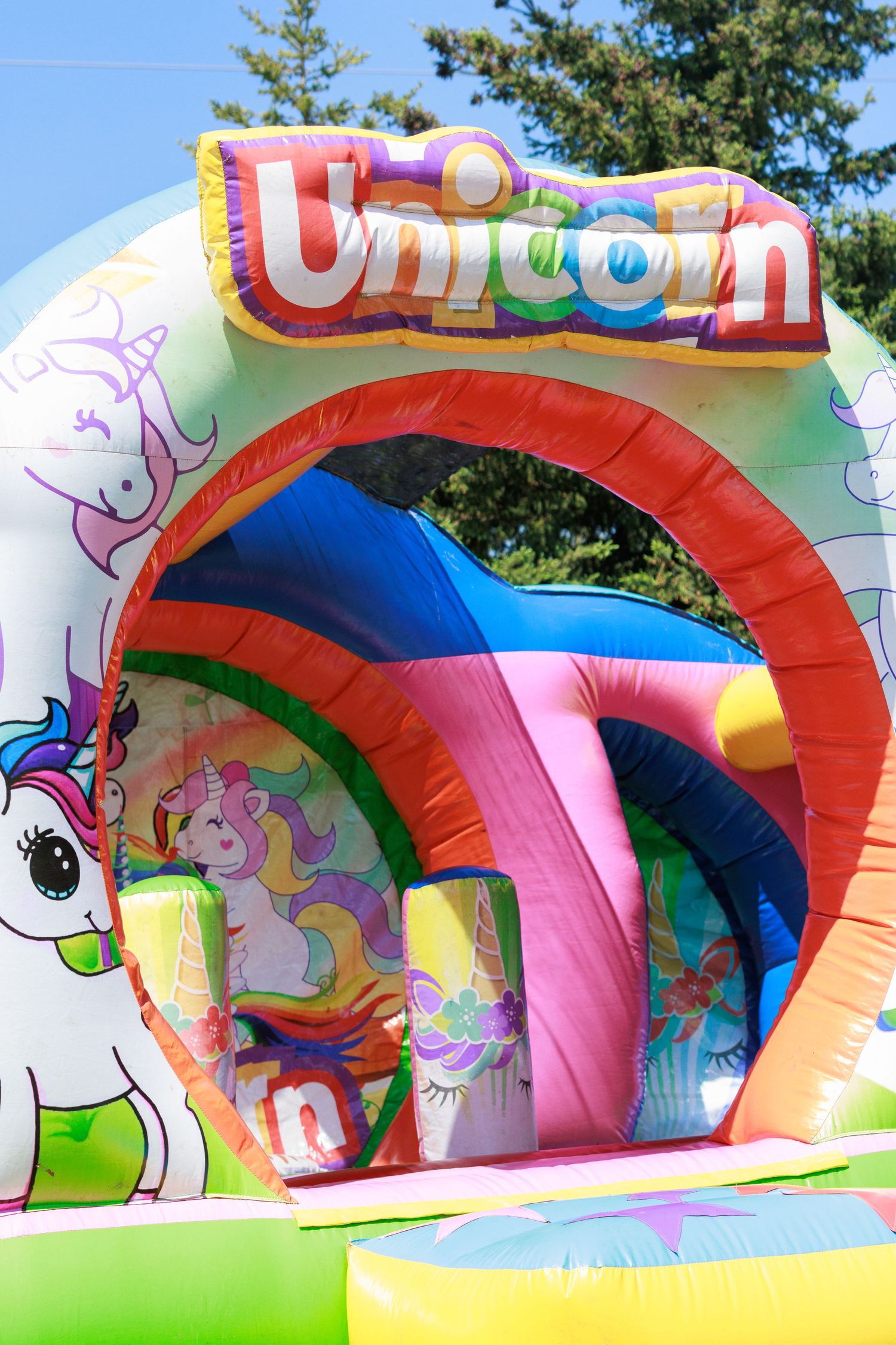 Colorful unicorn-themed inflatable bounce house with rainbow decorations.