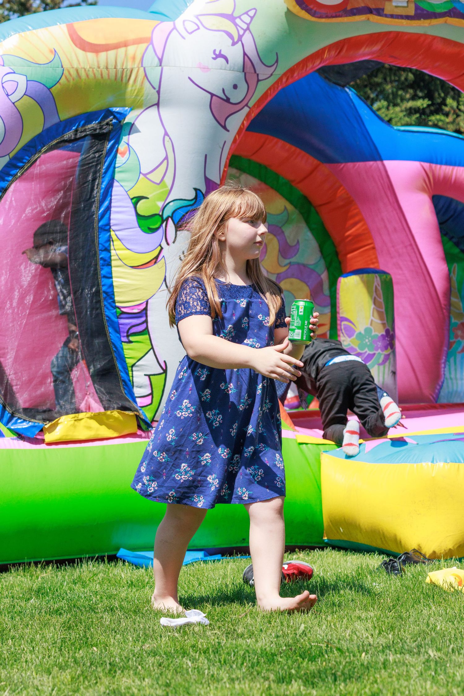Child in blue dress playing near colorful unicorn bounce house.