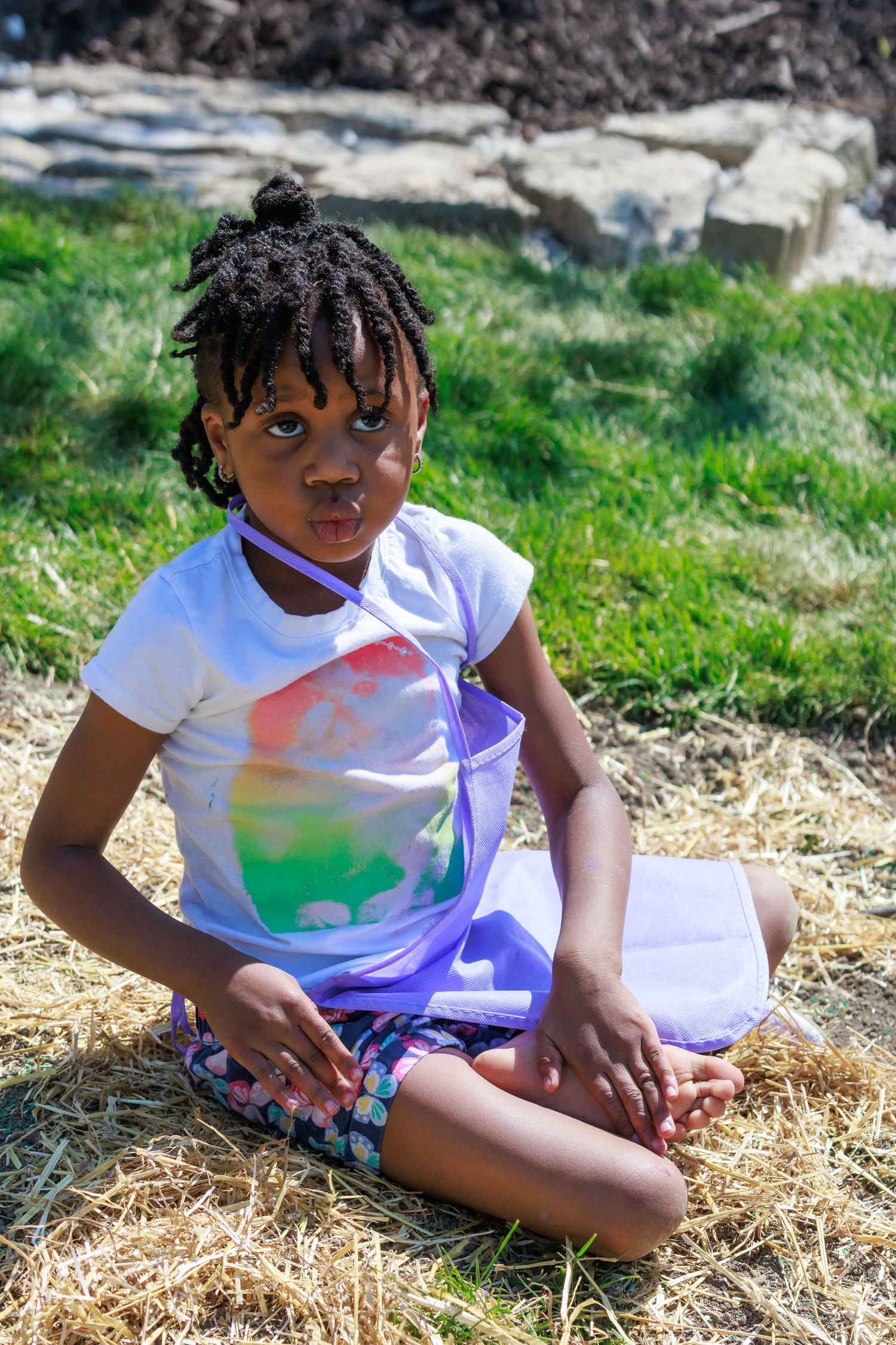 Youth sitting on grass wearing tie-dye shirt on sunny day.