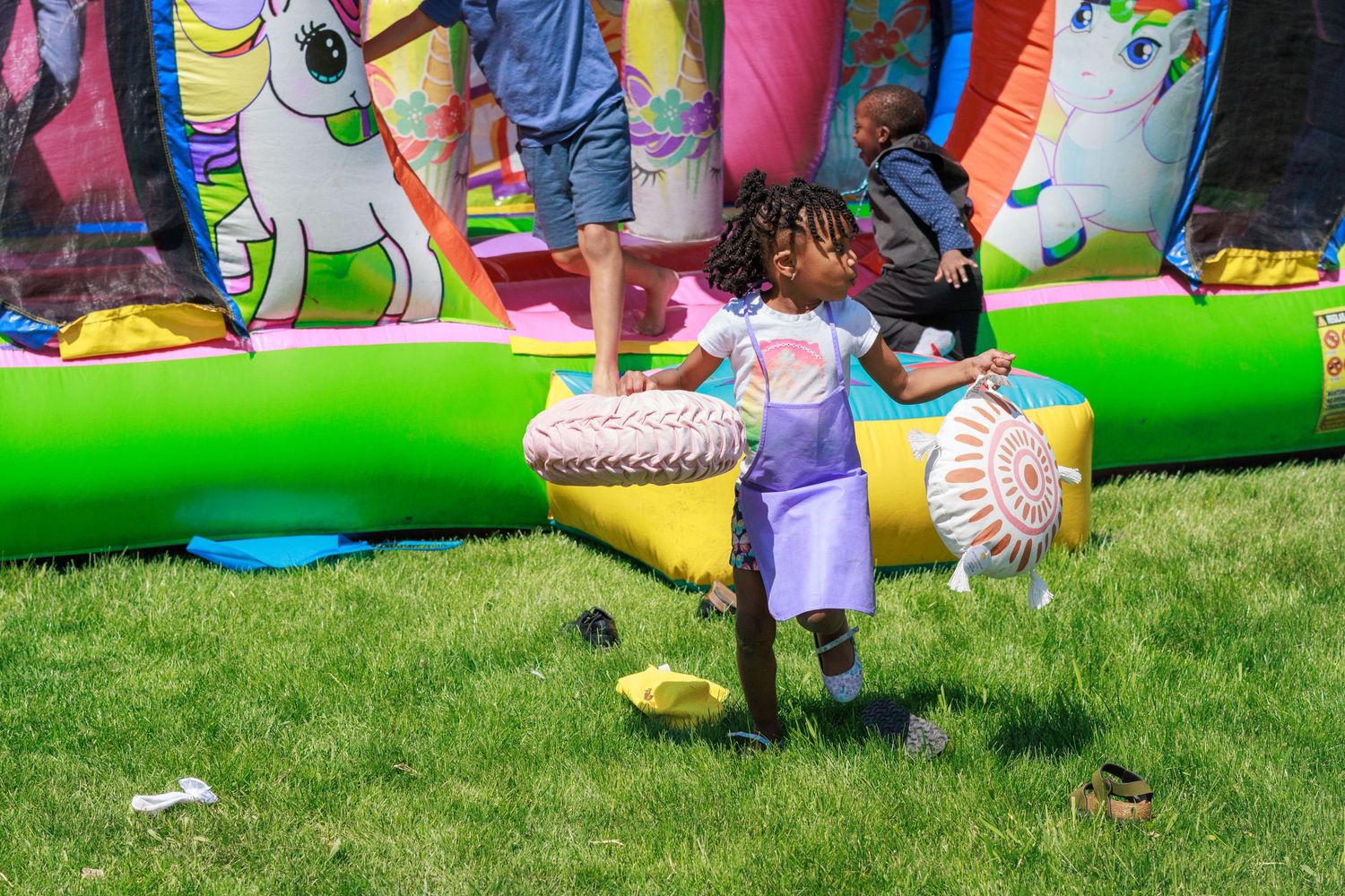 Child playing near colorful unicorn-themed bounce house on green grass.