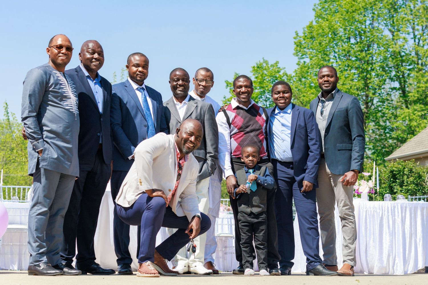Group of well-dressed men posing together at formal outdoor event.