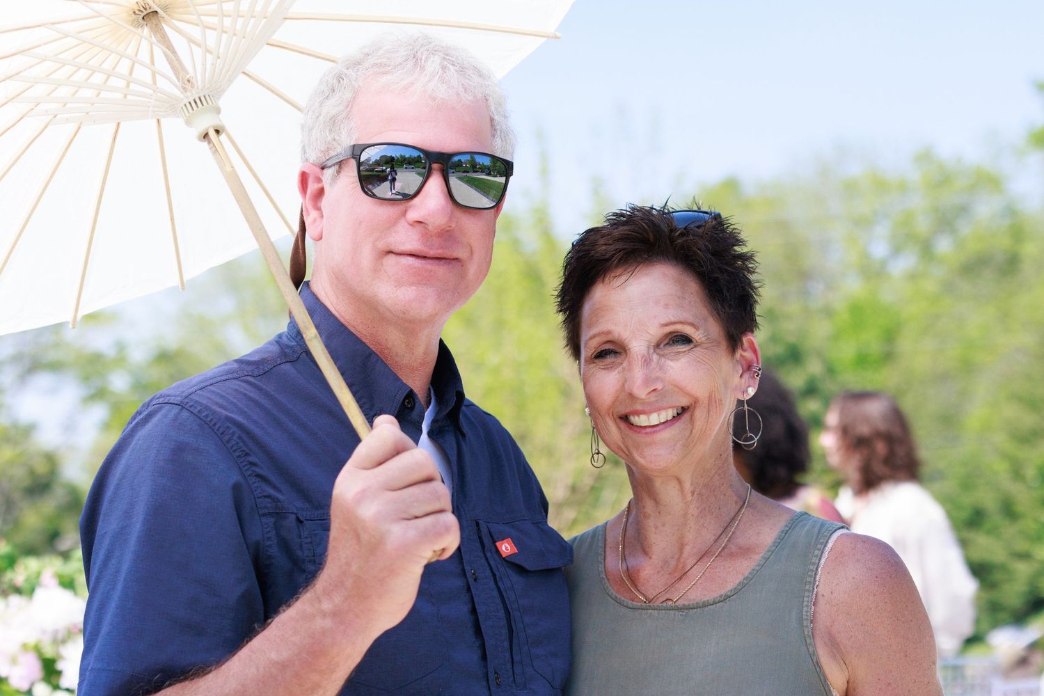 Couple holding white parasol at sunny outdoor gathering.