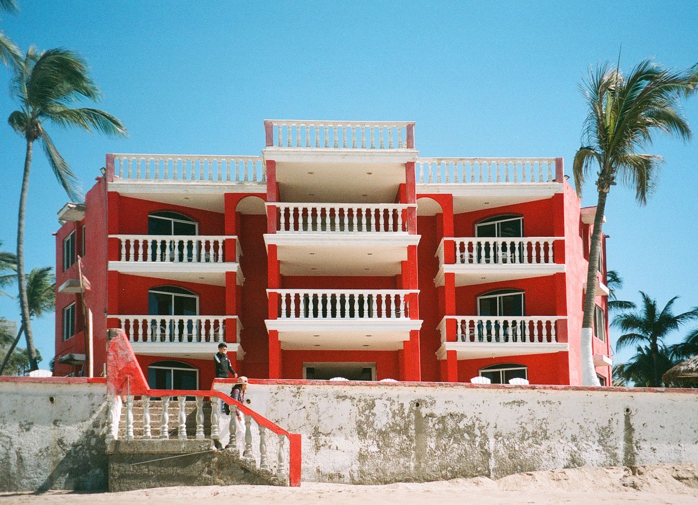 Coral-colored beachfront apartment building with white balconies and palm trees.