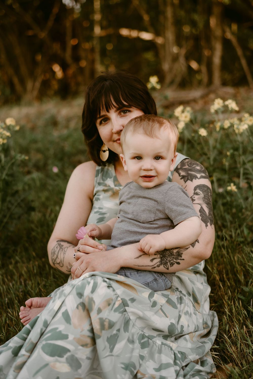 Outdoor portrait of parent and baby surrounded by blooming wildflowers.