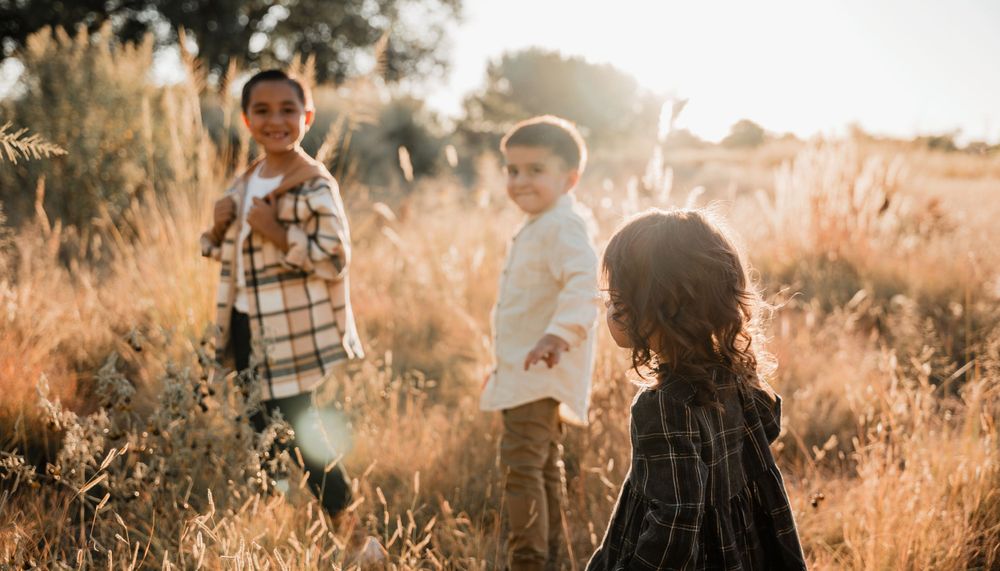 Natural outdoor family photoshoot with sun flare in a rustic field setting.