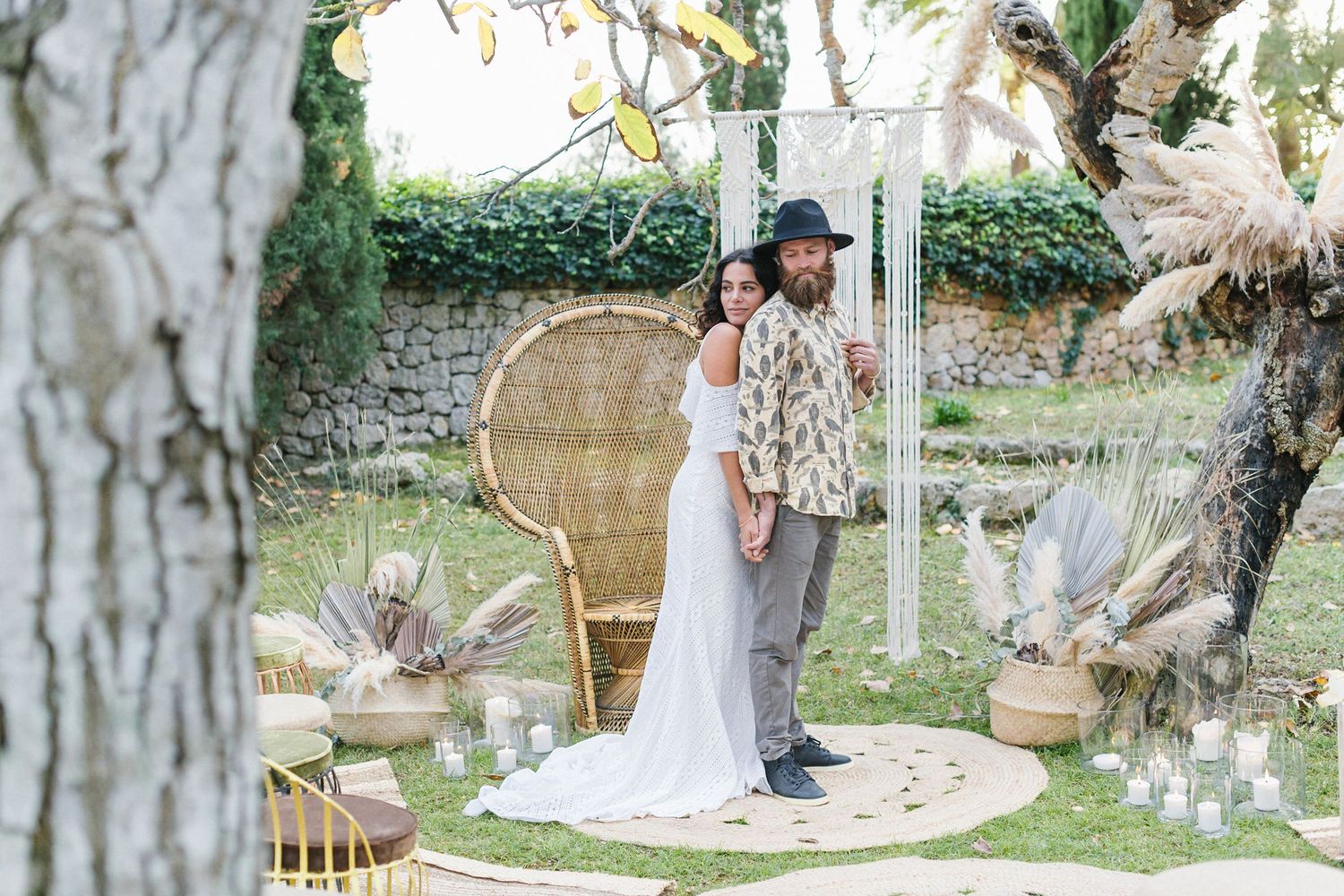 A bride embraces the groom surrounded by candles, pampas grass, a peacock chair and Macrame decor