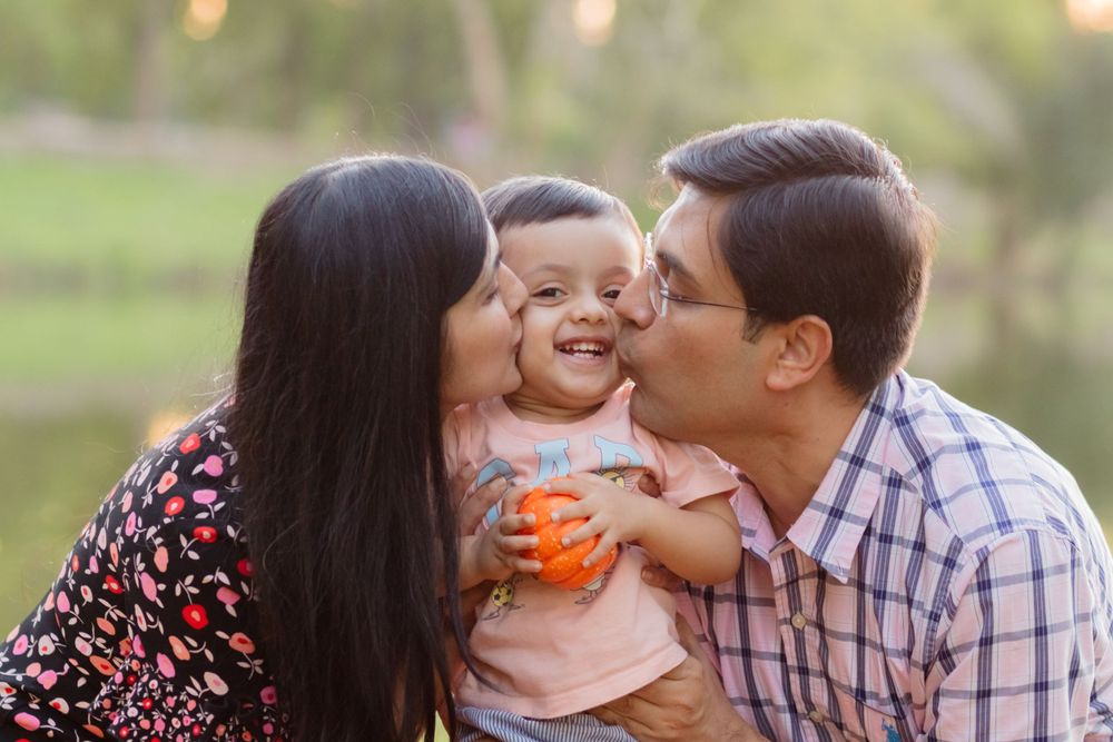 A happy family sharing affectionate kisses outdoors with a glowing sunset backdrop.