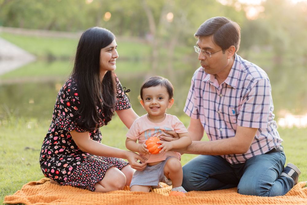 A young family sits on an orange blanket having a picnic by a lake at sunset.