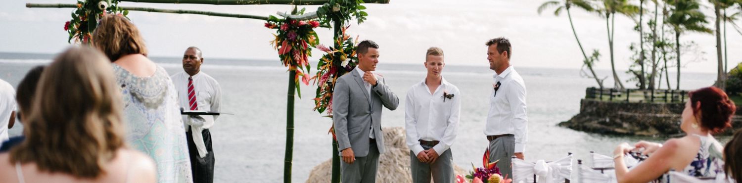 Wedding party gathered under floral arch during oceanside ceremony.