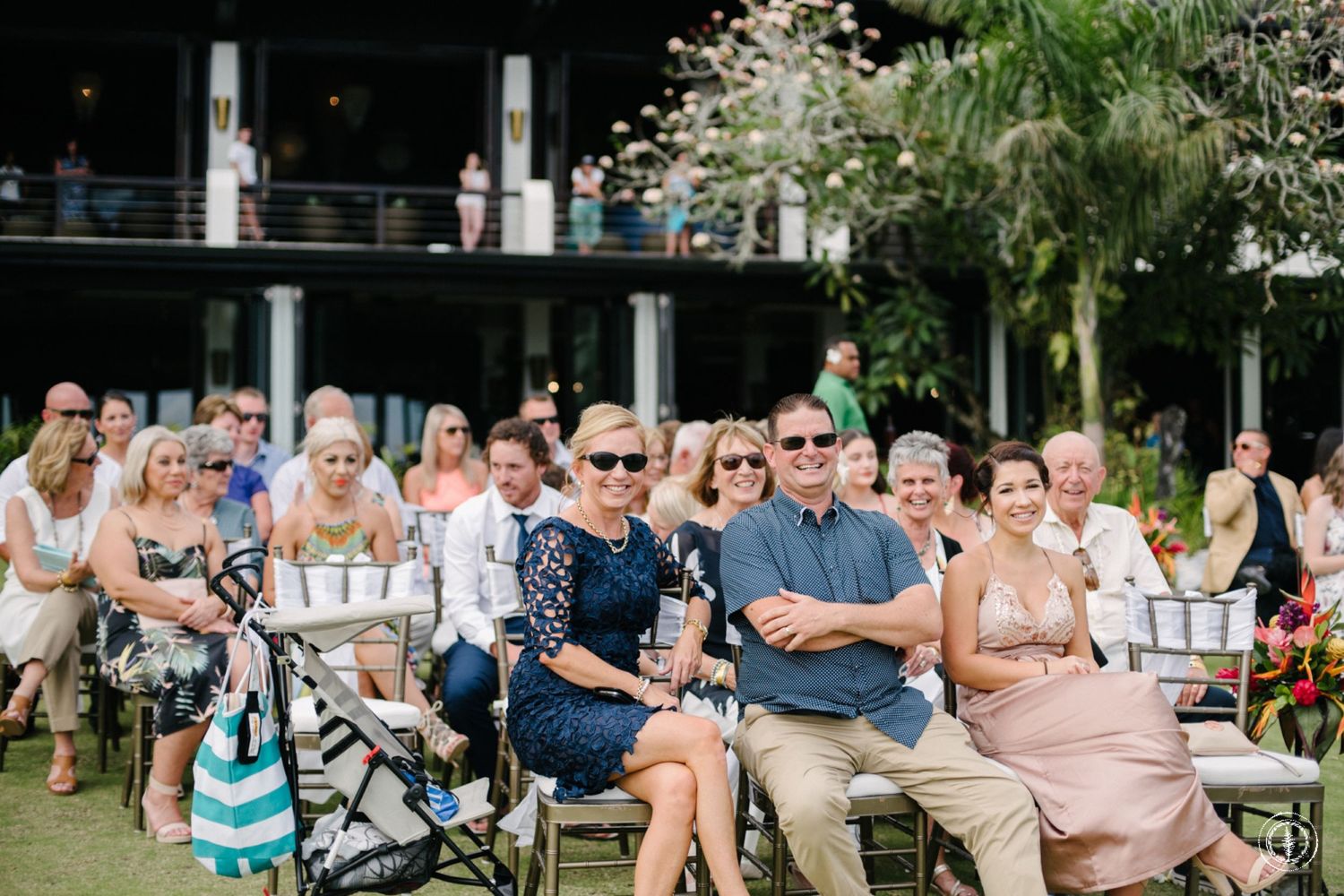 Wedding guests seated outdoors under palm trees at a tropical destination ceremony.