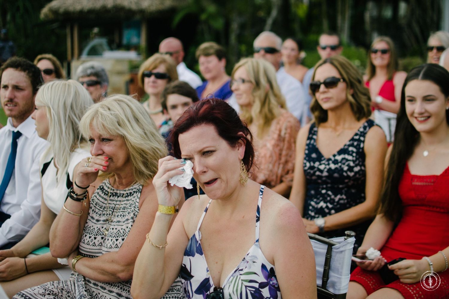 Wedding guests show emotional reactions while watching the ceremony from their seats.