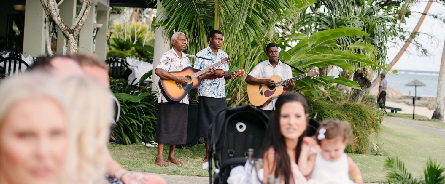 Musicians perform with guitars during an outdoor tropical wedding celebration.