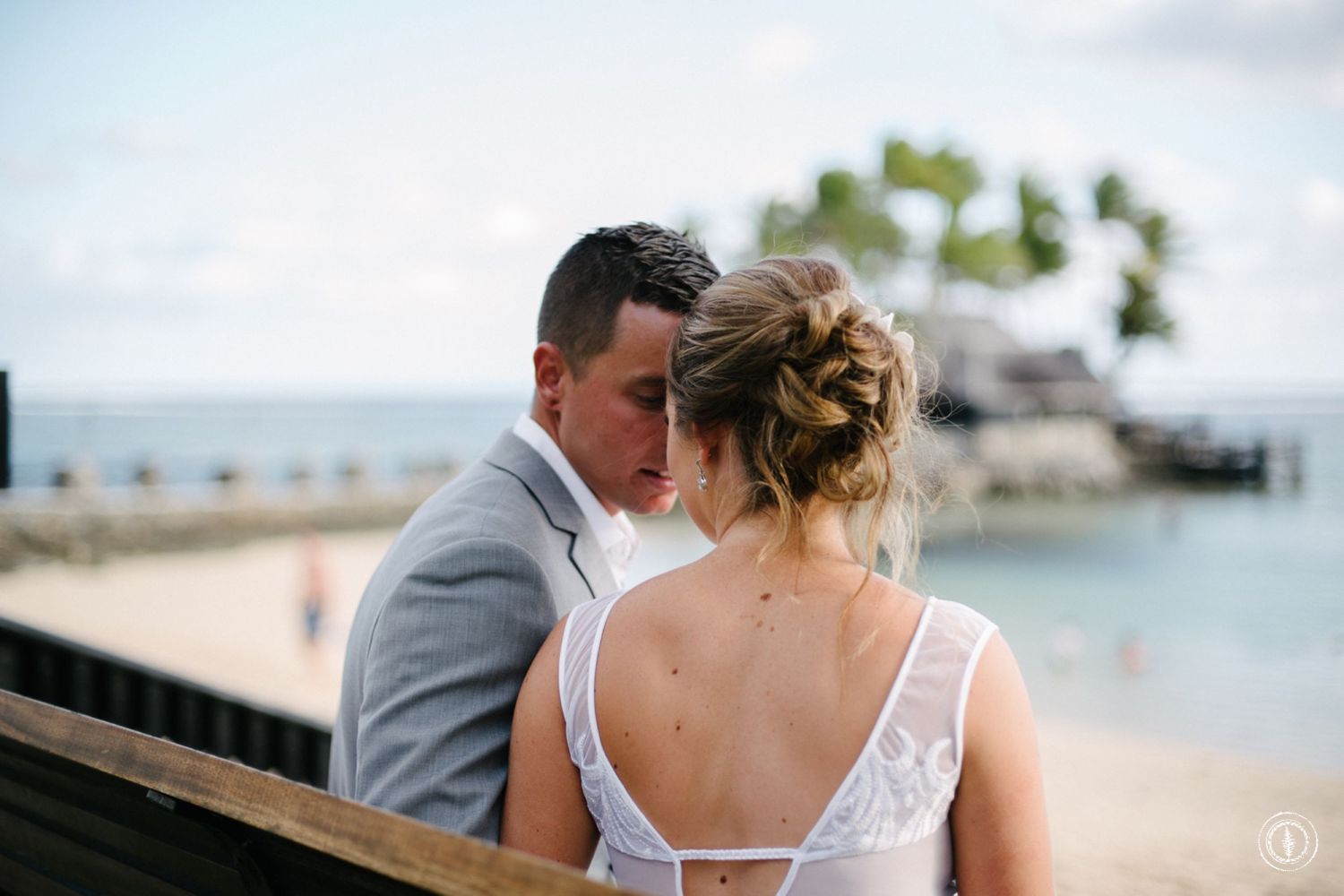 Romantic waterfront moment on wooden deck with tropical resort in background.