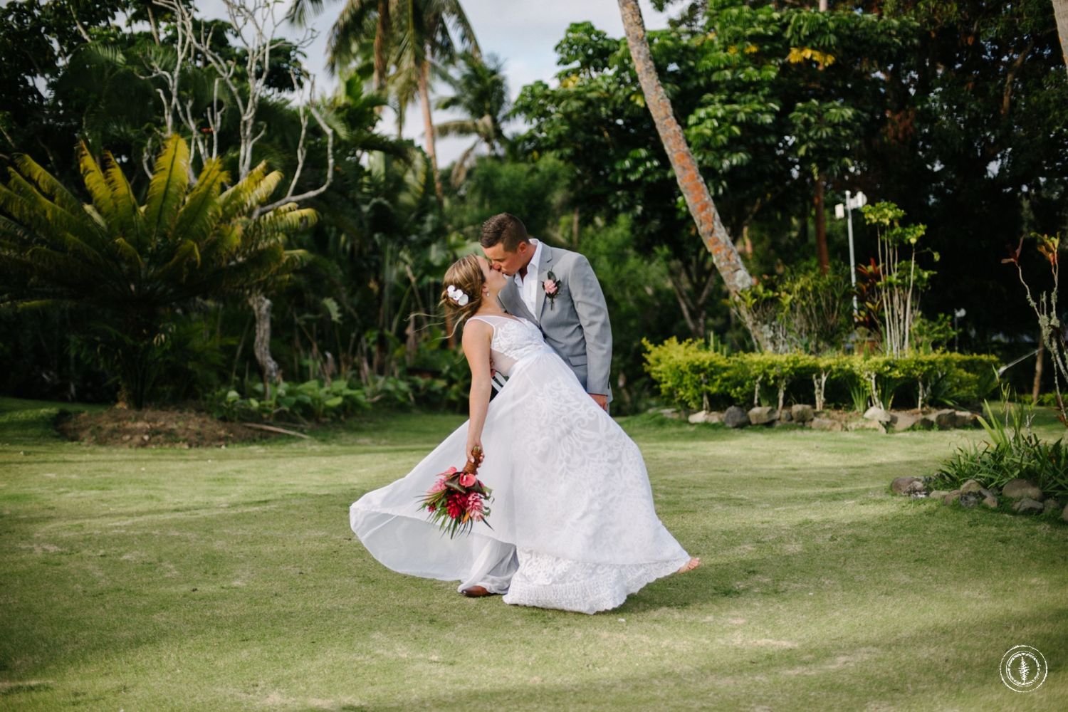 Dancing couple on manicured lawn surrounded by tropical landscaping and palm trees.