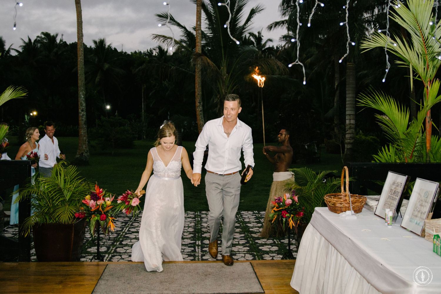 Couple walking together on illuminated pathway during tropical evening reception.