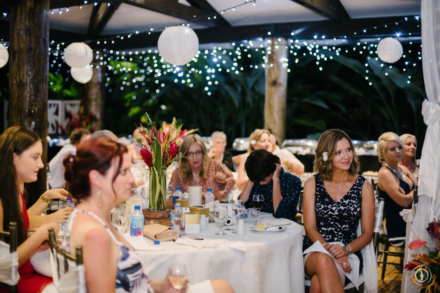 Reception guests seated at round tables under twinkle lights and paper lanterns.