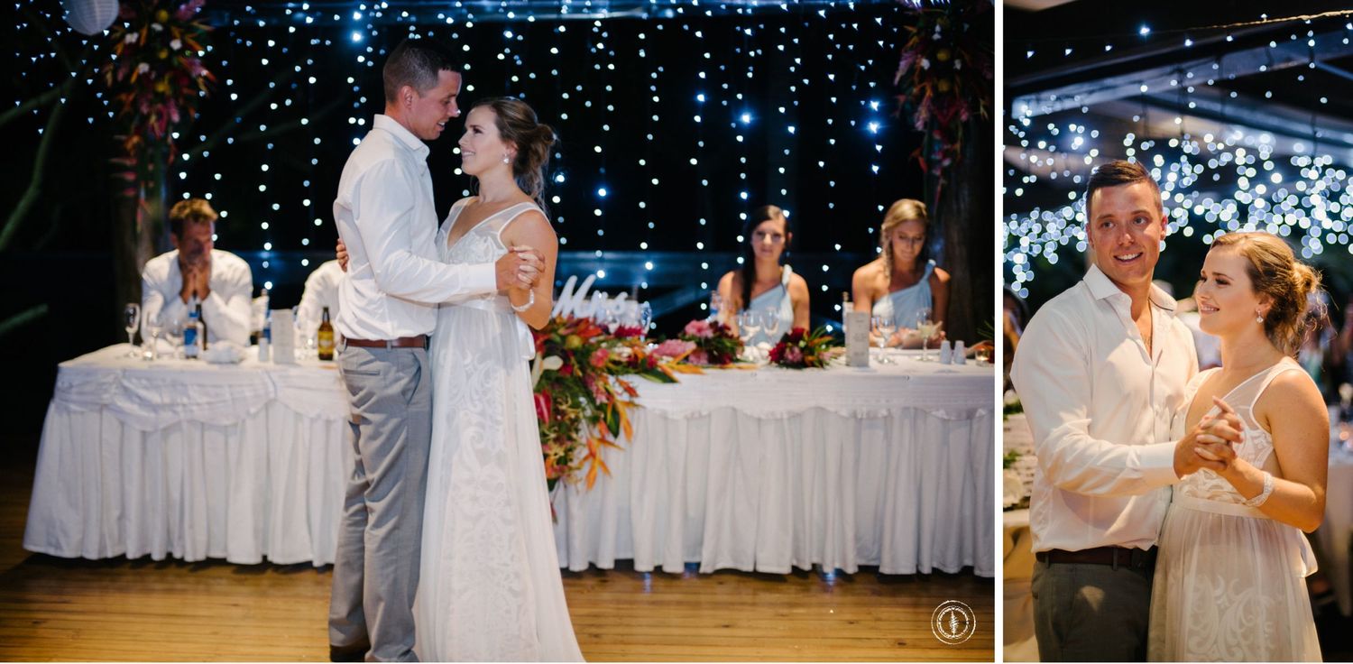 Wedding couple shares their first dance under twinkling lights with decorated reception tables in the background.