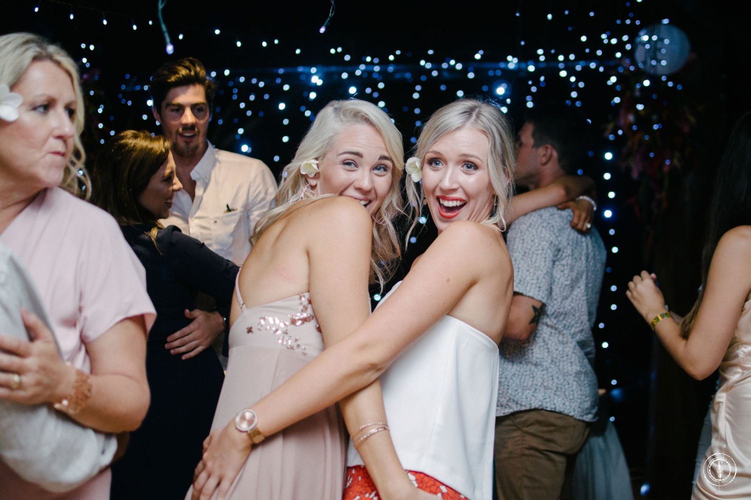 Wedding party members enjoy dancing and celebrating on the dance floor under string lights.