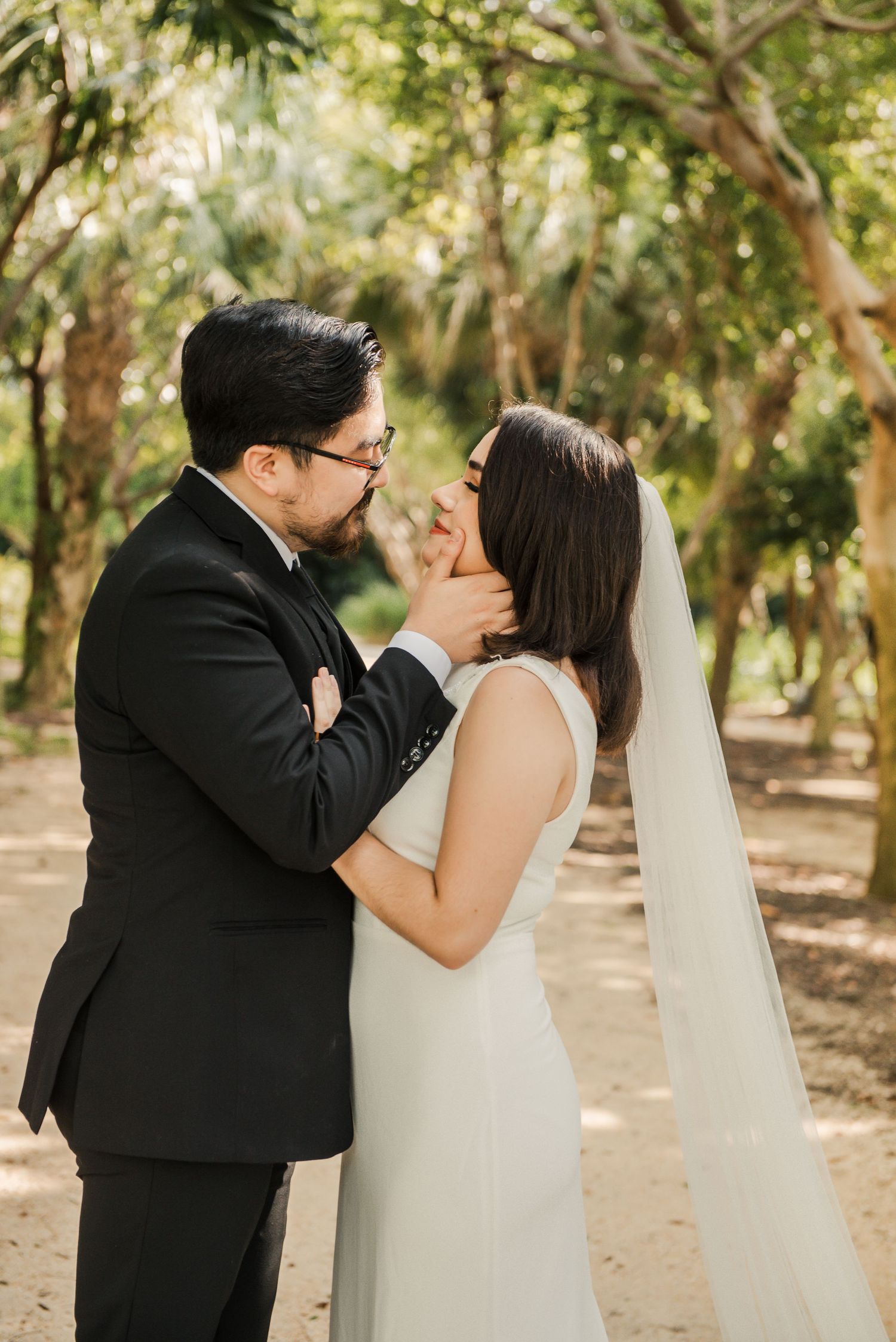 A tender moment between newlyweds amid a tree-lined path at a sunny outdoor wedding ceremony.