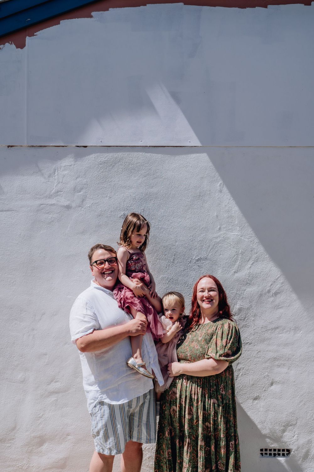 A family looking at the camera, standing in front of a wall of their family home