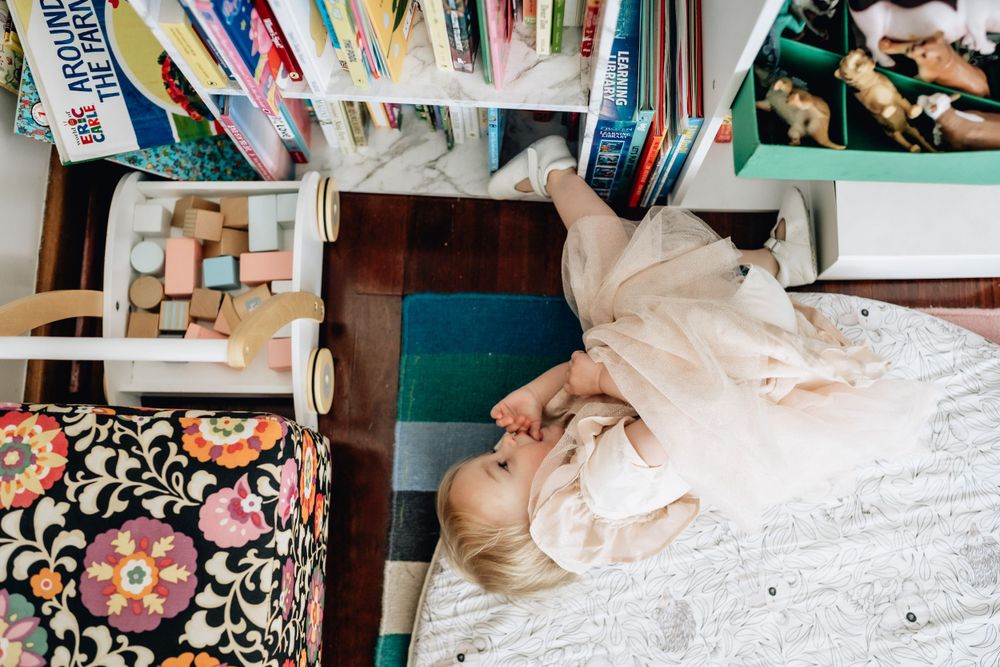 A Birds Eye view of a toddler curled up on the floor next to a bookcase