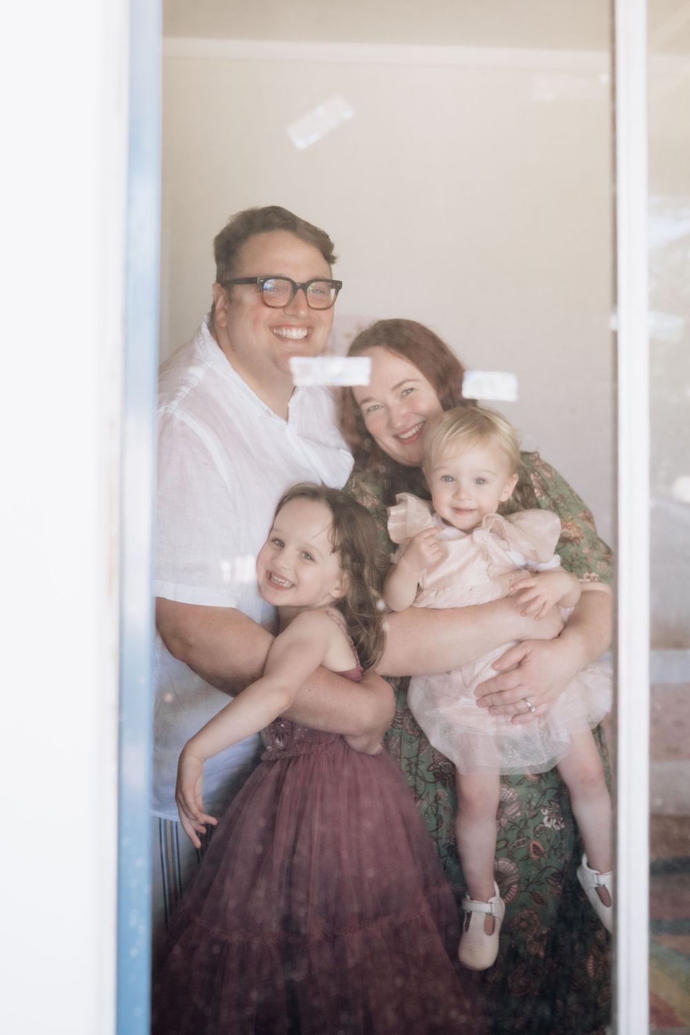 Mum, Dad and two daughters looking through a window at a photographer in Perth
