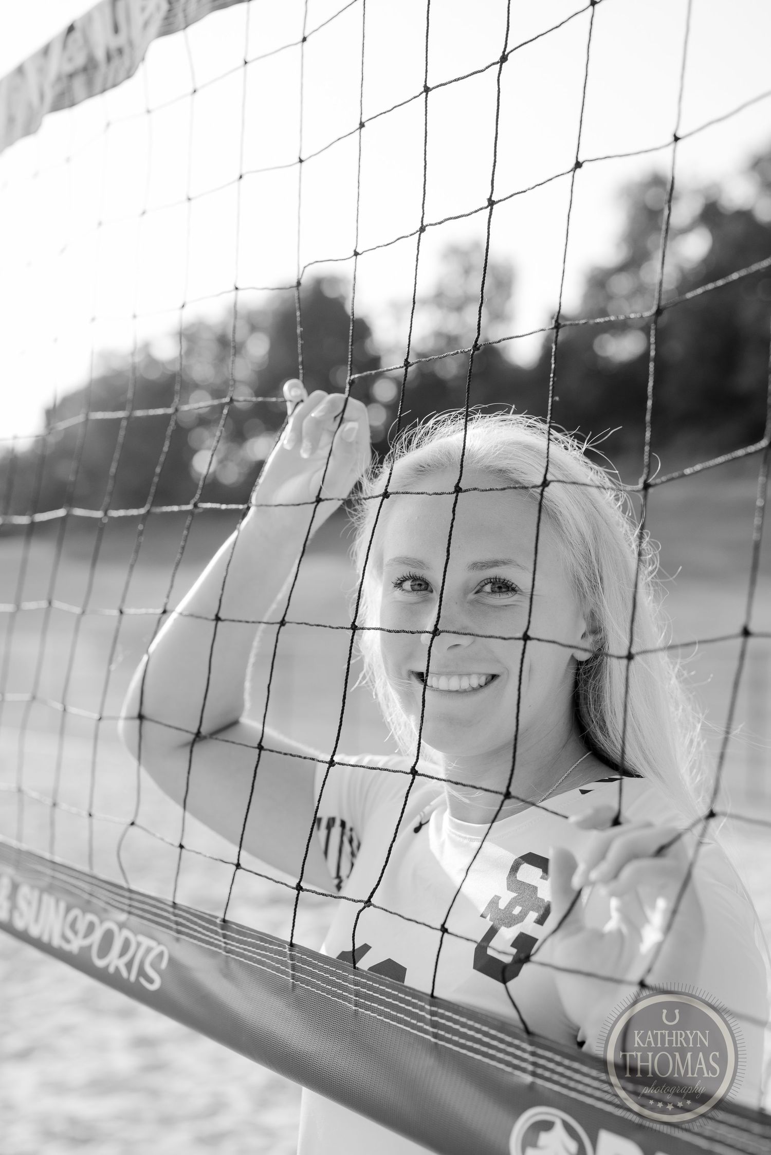 A black and white portrait through a volleyball net during golden hour lighting.