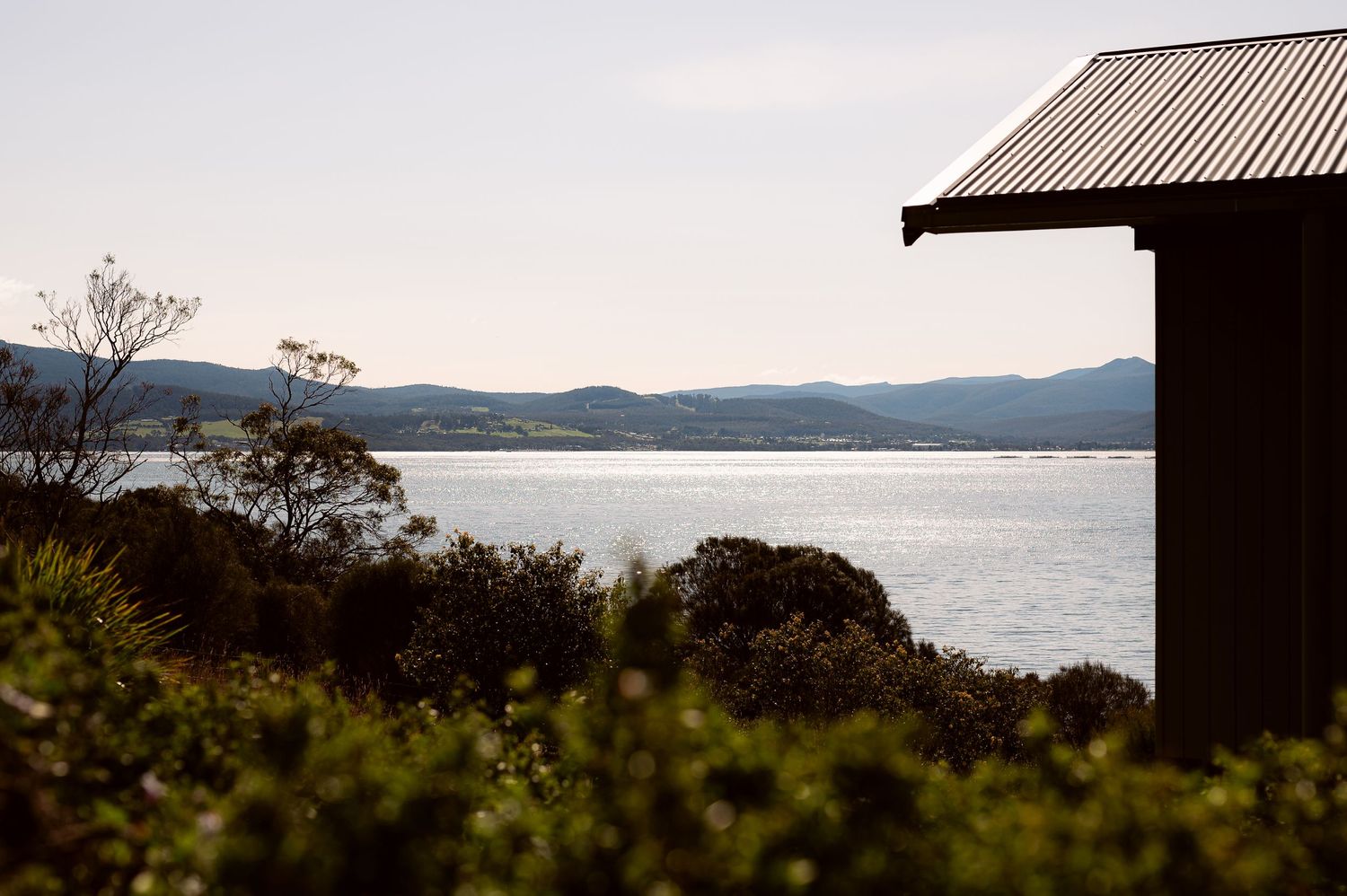 Scenic lakefront view with mountains and metal-roofed structure in foreground.
