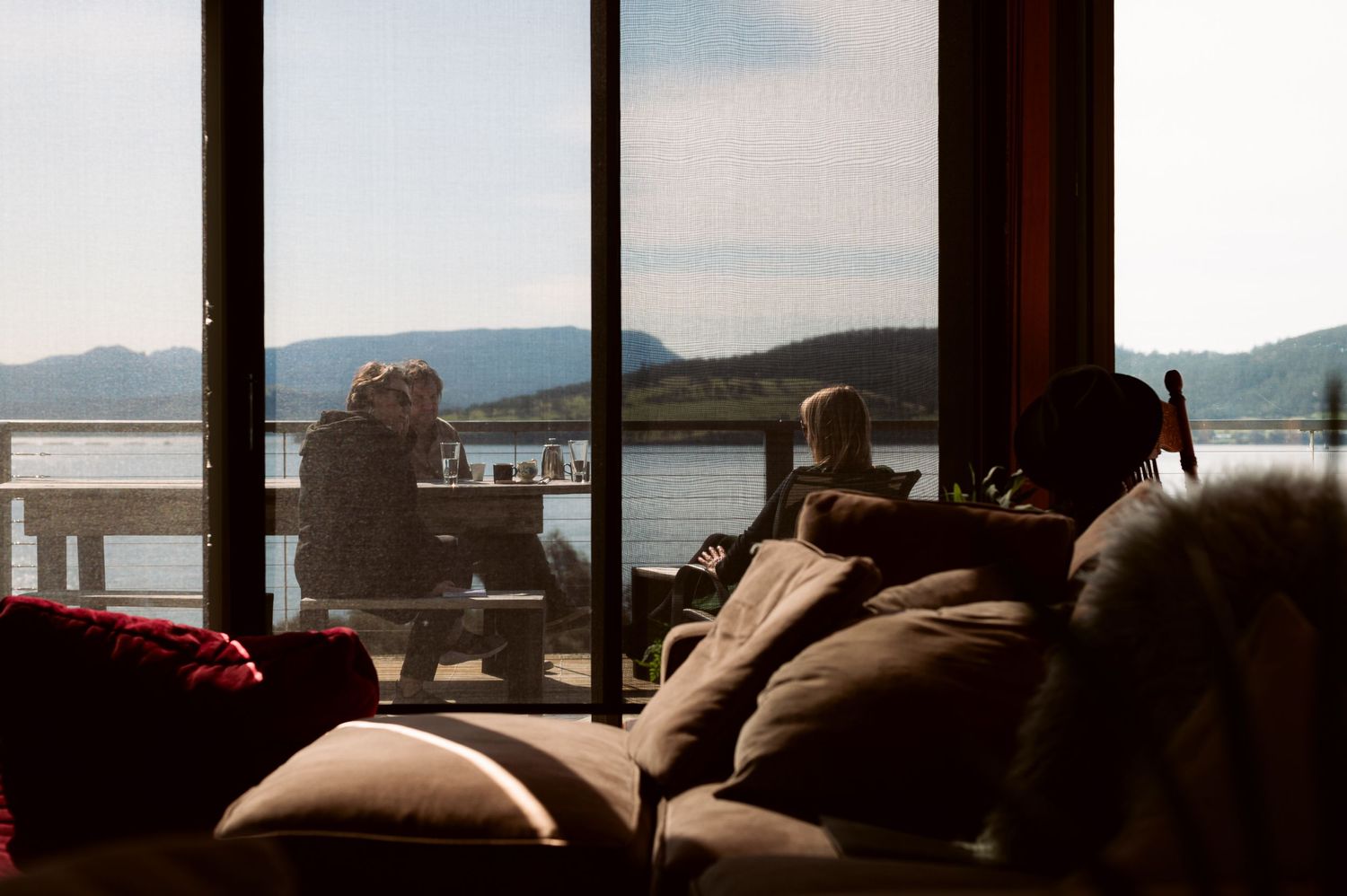 View of lake and mountains through large window with silhouetted furniture.