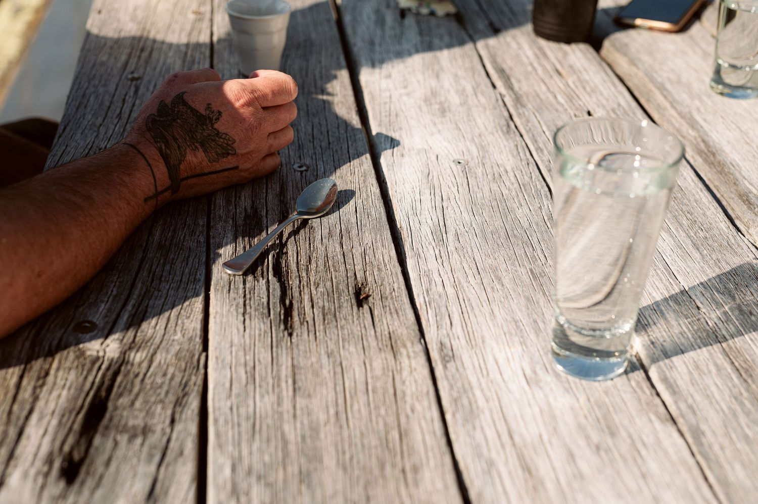 Close-up of hands resting on weathered wooden deck boards with glass of water.