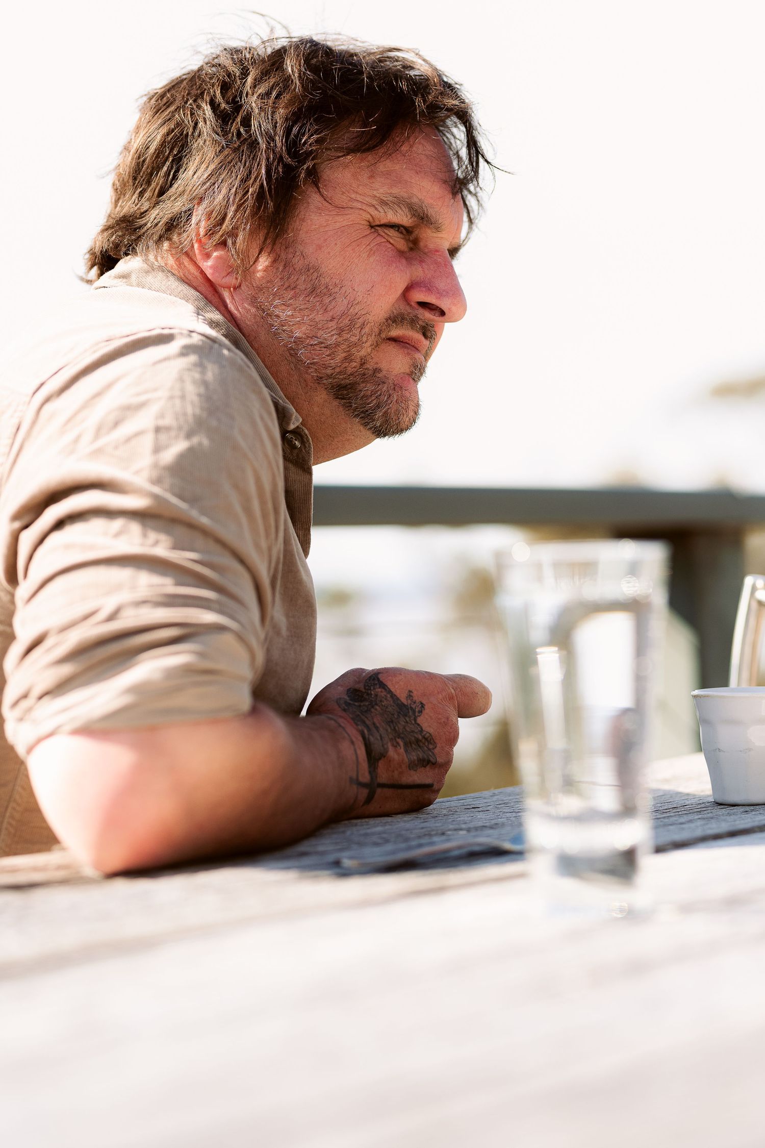 Person leaning on wooden table outdoors with glasses of water.