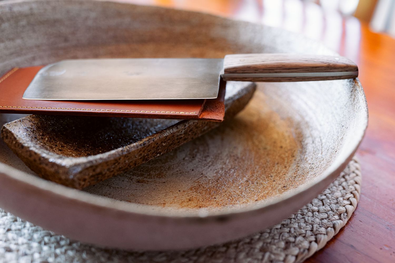 Close-up of knife resting on brown ceramic plate.