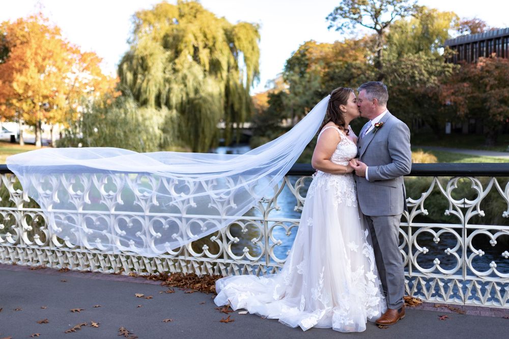 Bride and groom portrait veil in the air on a bridge with trees behind them