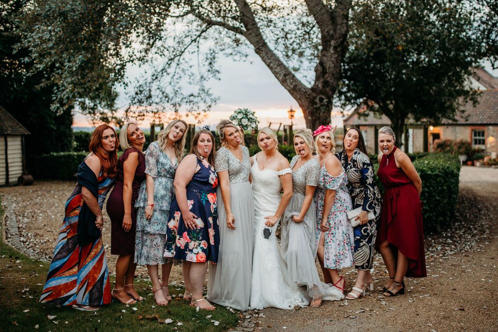 Wedding group photo outdoors with attendees wearing colorful floral dresses.