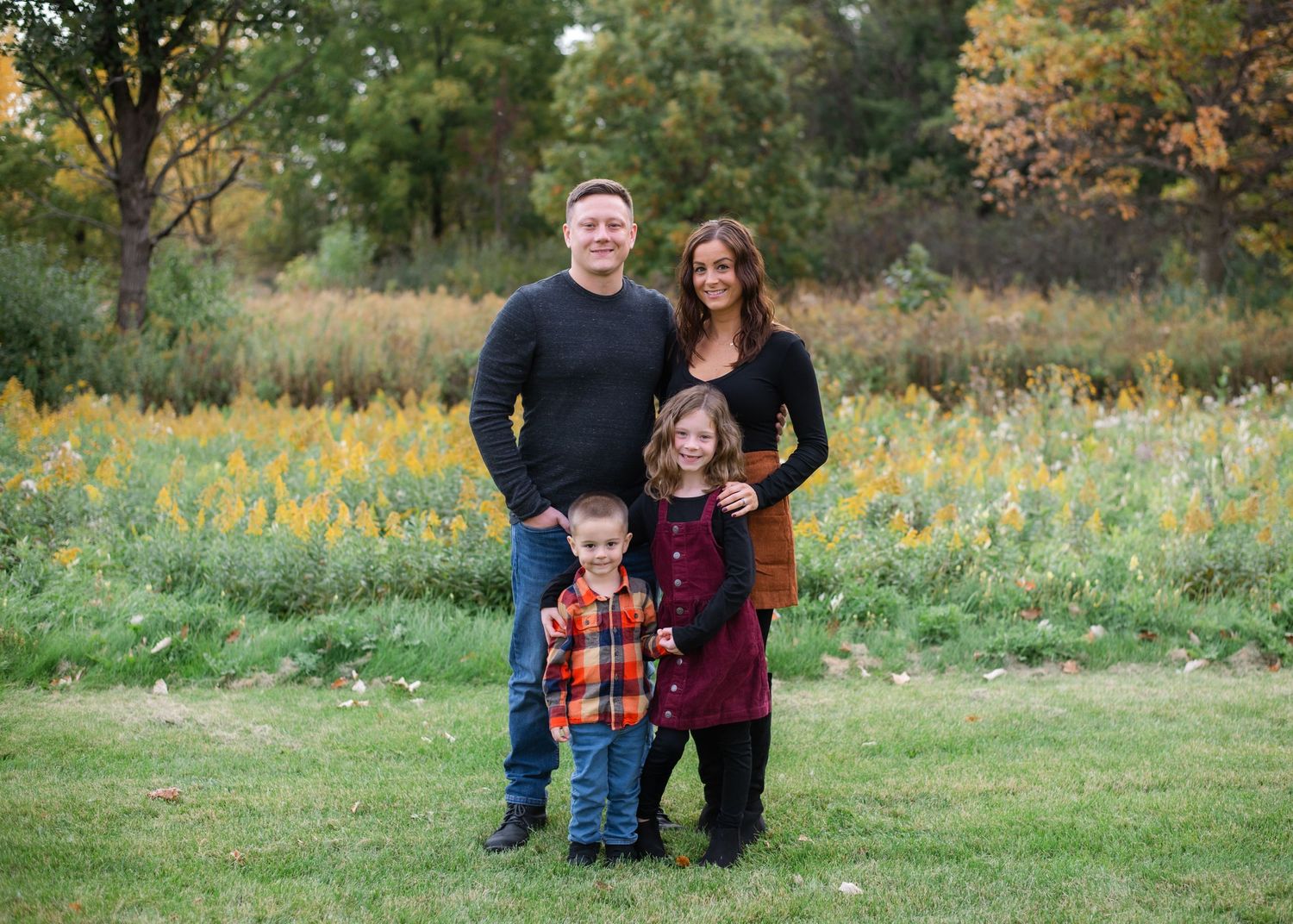 Family portrait in meadow with wildflowers and natural greenery backdrop.