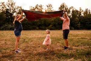 A playful family moment holding a red blanket in a sunny field.