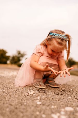 A small figure in a pink dress and tiara explores the ground with curiosity.